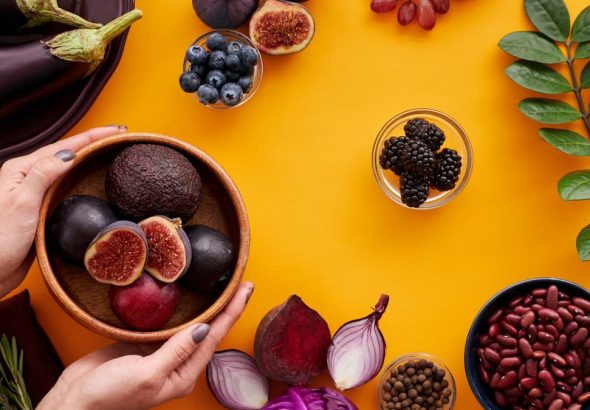 Colorful arrangement of fruits and vegetables on a yellow background, featuring figs and eggplants.
