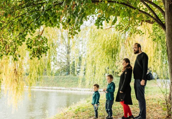 A family enjoys a peaceful walk by a lakeside under a willow tree during autumn.