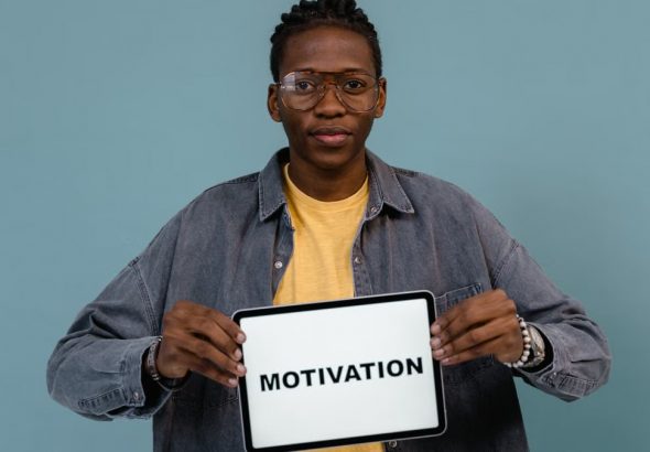 A young African American man holding a tablet displaying the word 'MOTIVATION' against a blue background.